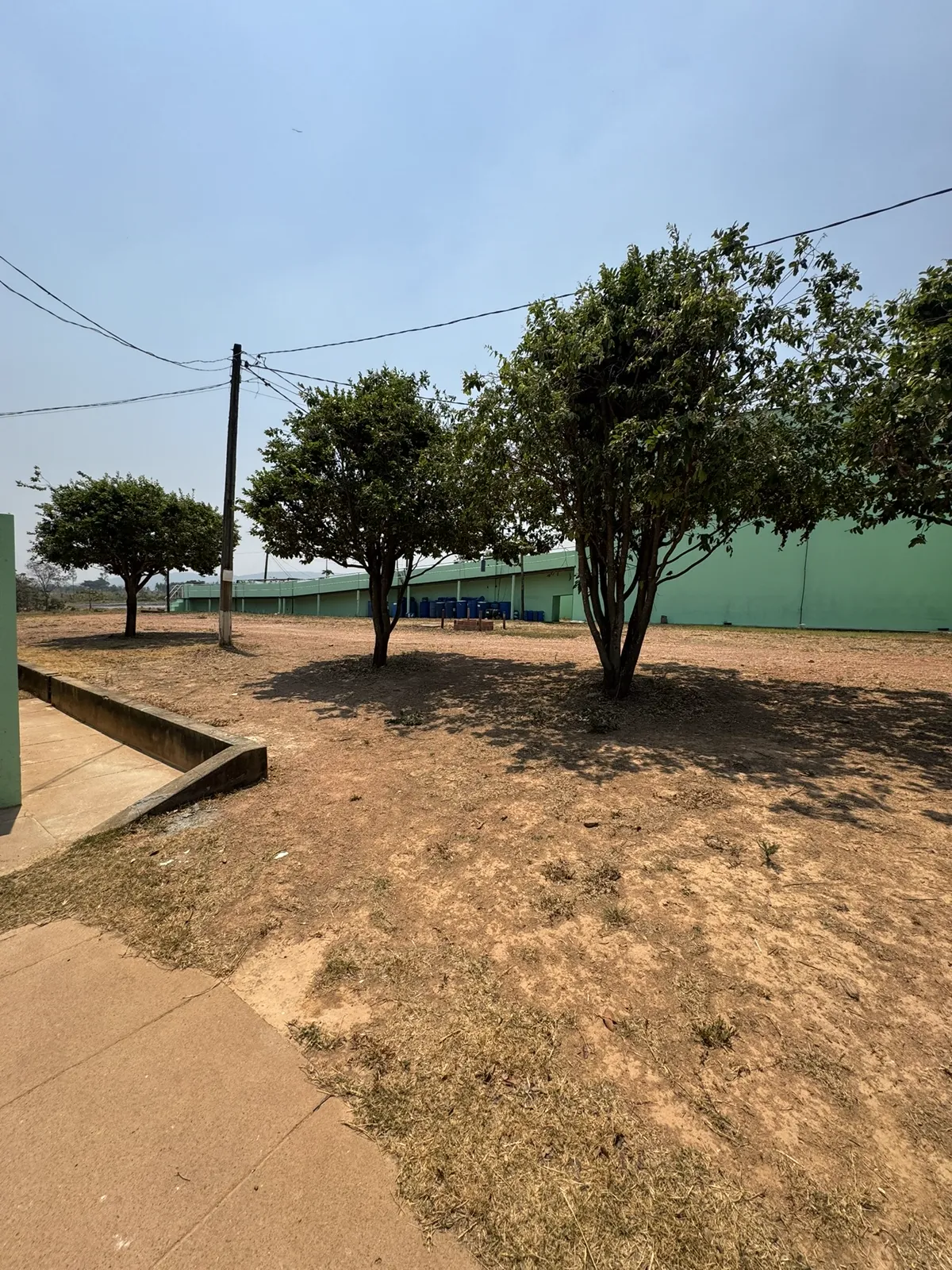 Vista externa do galpão industrial e do pátio arborizado.